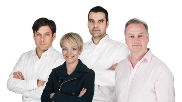 Eine Gruppe von vier Personen posiert vor einem weißen Hintergrund.