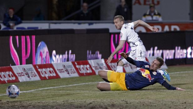 Ein Fußballspieler liegt auf dem Rasen, während ein anderer Spieler auf ihn zuläuft.