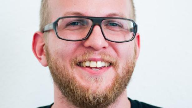 Ein lächelnder Mann mit Bart und Brille vor einem weißen Hintergrund.
