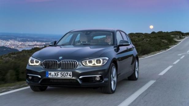 Ein grauer BMW fährt auf einer Landstraße in Richtung einer Stadt im Hintergrund.