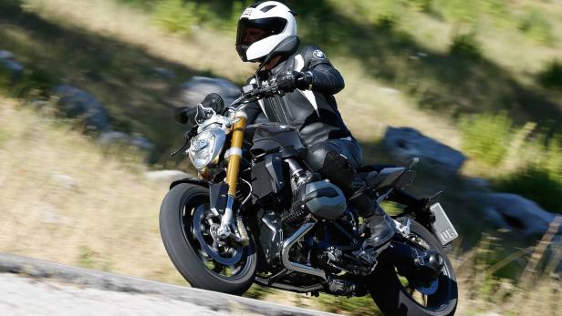 Ein Motorradfahrer in Lederkombi und Helm fährt auf einer kurvigen Straße.