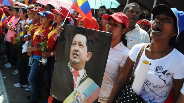 Eine Menschenmenge demonstriert mit venezolanischen Flaggen und einem Bild von Hugo Chávez.