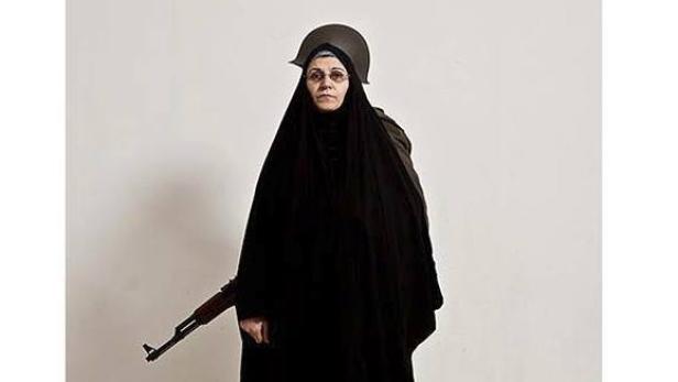 Eine Frau in einem schwarzen Tschador und einem Helm hält ein Gewehr.