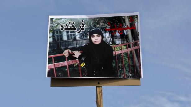 Ein Plakat mit dem Bild einer Frau mit Kopftuch vor blauem Himmel.