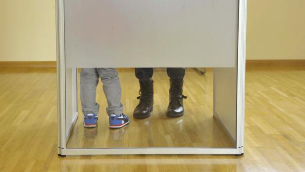 Die Füße eines Erwachsenen und eines Kindes in einer Wahlkabine.