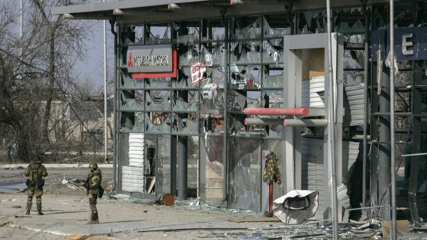 Zwei Soldaten stehen vor einem zerstörten Mitsubishi Autohaus.