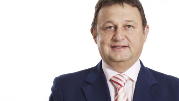 Ein Mann mit blauem Anzug und gestreifter Krawatte lächelt in die Kamera.