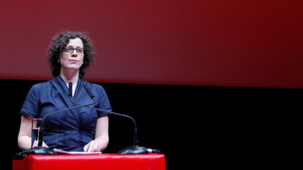 Eine Frau mit Brille steht an einem Rednerpult vor einem roten Hintergrund.