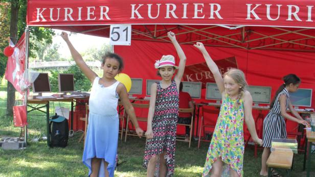 Drei Mädchen stehen vor einem Stand des „Kurier“ und jubeln.