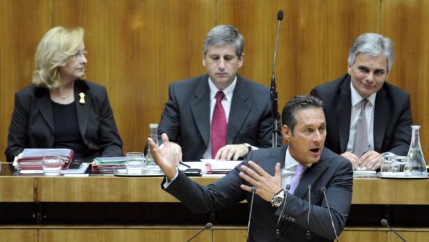 Ein Mann gestikuliert während einer Rede vor drei weiteren Personen.