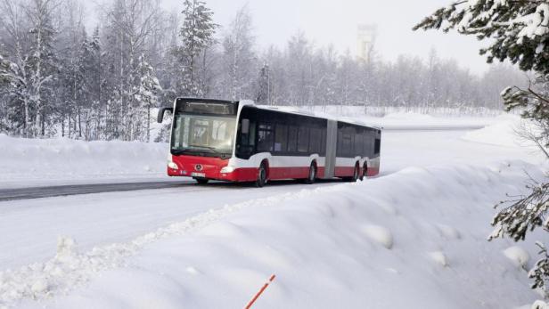 Ein rot-weißer Gelenkbus fährt auf einer verschneiten Straße.