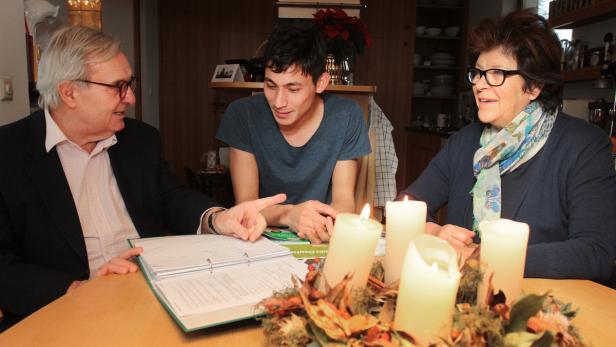 Drei Personen sitzen an einem Tisch mit Adventskerzen und betrachten ein Dokument.