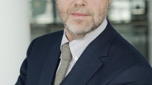 Ein Mann mit Brille, Anzug und verschränkten Armen blickt in die Kamera.