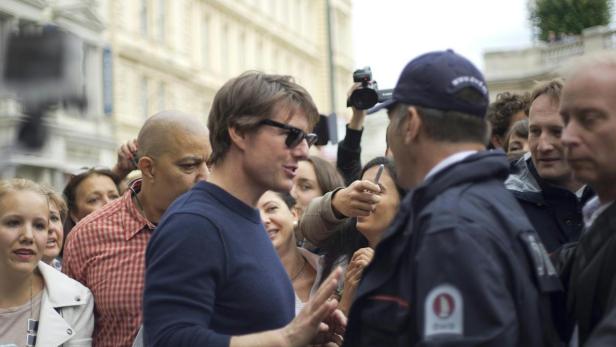Tom Cruise interagiert mit Fans und Sicherheitskräften in einer städtischen Umgebung.