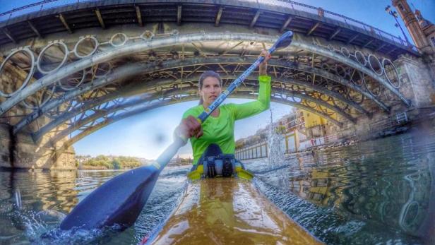 Eine Frau paddelt mit einem Kajak unter einer Brücke hindurch.