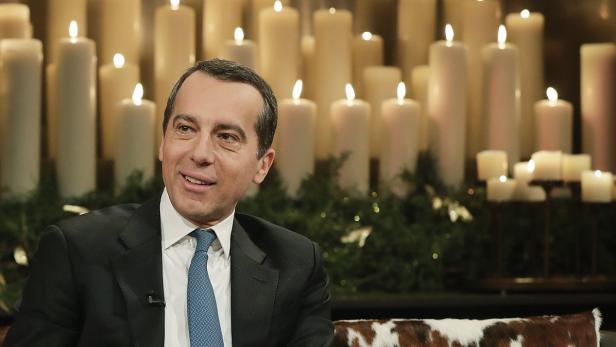 Ein Mann im Anzug sitzt vor einem Hintergrund aus brennenden Kerzen.