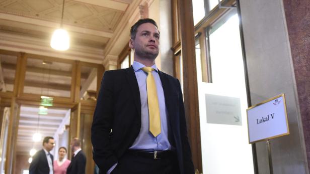 Ein Mann in Anzug und gelber Krawatte geht in einem Gebäude entlang.