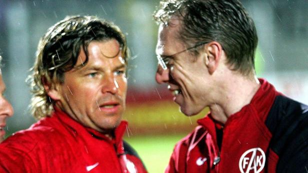 Zwei Männer in roten Jacken stehen im Regen und unterhalten sich.