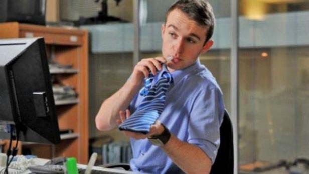 Ein Mann im Büro bindet seine blau-gestreifte Krawatte.