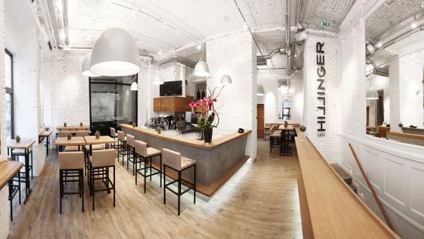 Innenansicht des Restaurants „HIllinger LEO“ mit Bar, Tischen und weiß gestrichenen Ziegelwänden.