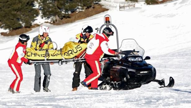 Rettungskräfte transportieren eine verletzte Person mit einer Trage zu einem Schneemobil.