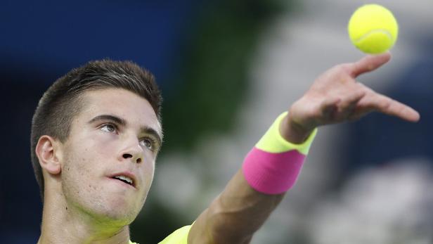 Ein Tennisspieler wirft einen gelben Tennisball in die Luft.