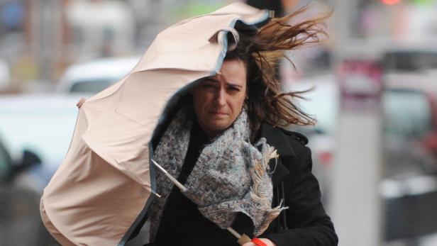 Eine Frau kämpft mit einem Regenschirm im starken Wind.