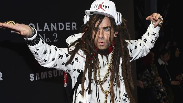 Ein Mann mit Dreadlocks, weißer Kappe und Kopfhörern posiert mit Ringen an den Fingern.