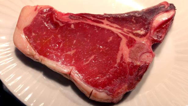 Ein rohes T-Bone-Steak liegt auf einem weißen Teller.