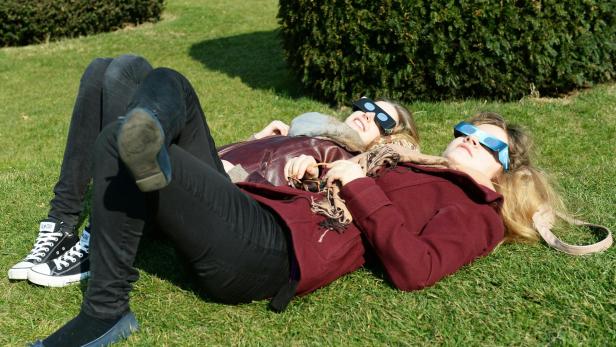 Zwei Frauen liegen mit Sonnenfinsternisbrillen auf einer Wiese.