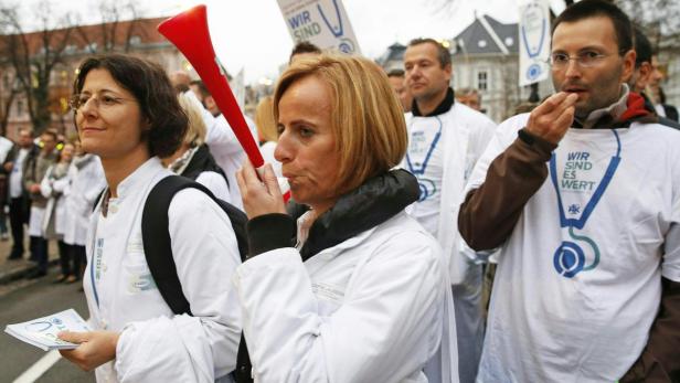 Ärzte demonstrieren mit Tröten und Schildern für bessere Arbeitsbedingungen.