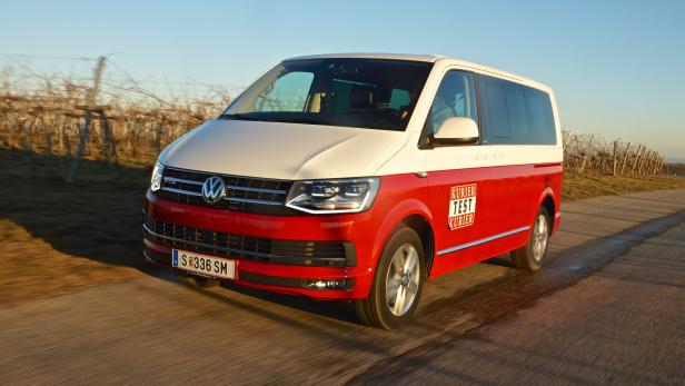 Ein rot-weißer VW-Bus fährt auf einer Landstraße.