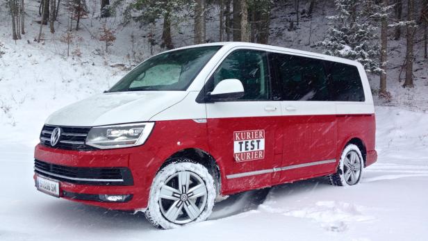 Ein rot-weißer VW-Bus fährt durch eine verschneite Winterlandschaft.