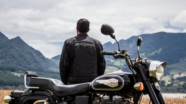 Ein Mann steht neben einem Royal Enfield Motorrad mit Blick auf eine Berglandschaft.