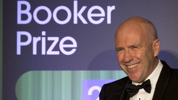Ein lächelnder Mann im Anzug steht vor dem Schriftzug „Booker Prize“.
