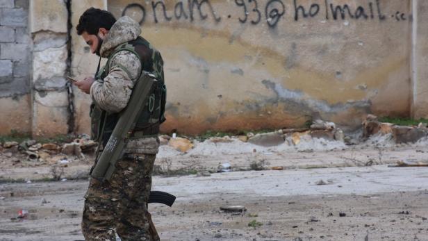 Ein Soldat in Tarnkleidung benutzt sein Handy in einer zerstörten Umgebung.