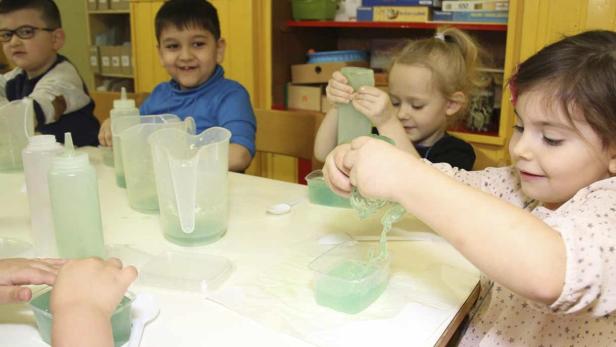 Eine Gruppe von Kindern spielt mit einer schleimigen, grünen Substanz an einem Tisch.