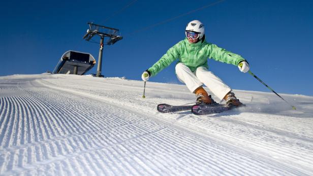 Eine Skifahrerin fährt auf einer präparierten Piste an einem Skilift vorbei.