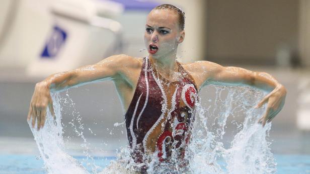 Eine Synchronschwimmerin im Wasser, umgeben von Spritzwasser.