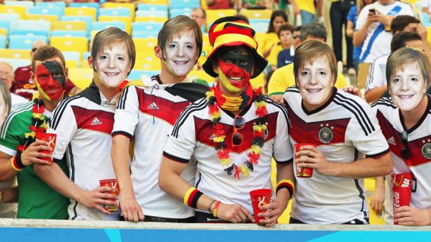 Deutsche-Fans mit einer Angela Merkel-Maske. Die Bundeskanzlerin ist für die deutsche Nationalmannschaft ein Glücksbringer. Lediglich zwei Spiele der deutschen Elf bei Welt-oder Europameisterschaften verloren die Deutschen, wenn Merkel das Spiel auf der Tribüne mitverfolgte.