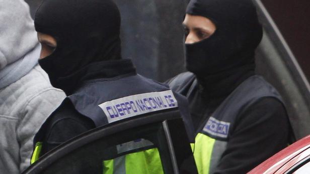 Zwei spanische Polizisten mit Sturmhauben stehen neben einem Auto.