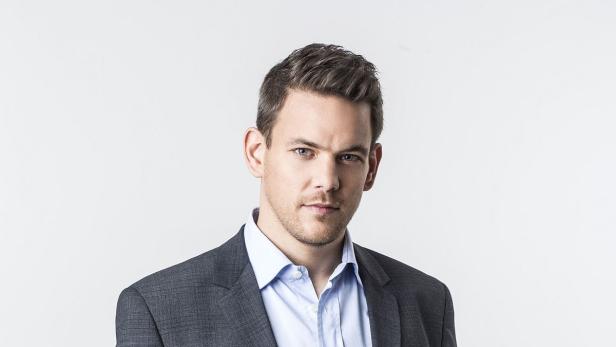 Ein Mann mit Anzug und hellblauem Hemd vor einem weißen Hintergrund.