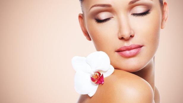 Eine Frau mit geschlossenen Augen und einer weißen Orchidee auf der Schulter.