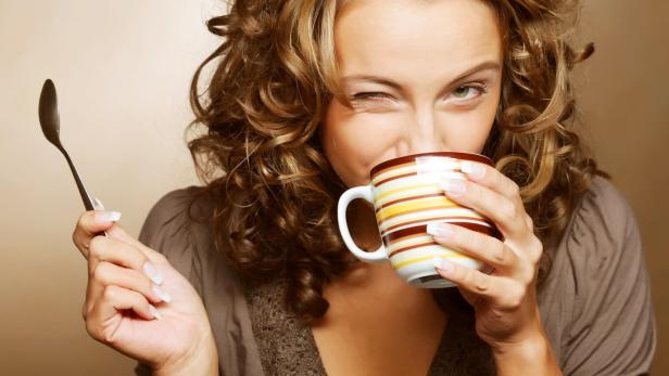 Eine Frau mit lockigem Haar trinkt aus einer gestreiften Tasse und zwinkert.