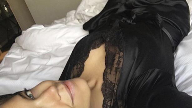 Eine Frau liegt in einem schwarzen Negligé auf einem Bett.