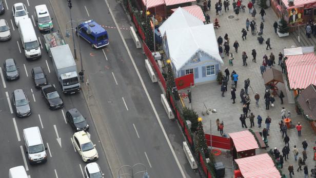 Blick von oben auf einen Weihnachtsmarkt neben einer belebten Straße mit Autos und Buden.