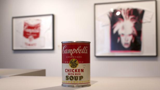 Eine Dose Campbell's Hühnersuppe mit Reis steht vor zwei gerahmten Kunstwerken.