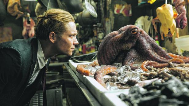 Ein Mann im Anzug betrachtet einen großen Oktopus auf einer Fischtheke.