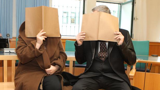 Zwei Personen verdecken ihre Gesichter mit Aktenordnern in einem Gerichtssaal.