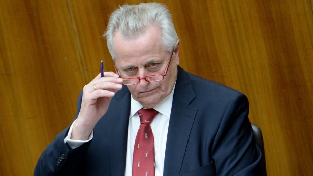 Ein Mann mit Anzug und Krawatte hält eine Brille in der Hand.